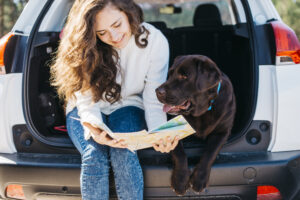 Cachorro sentado ao lado da sua tutora no porta-malas do carro.